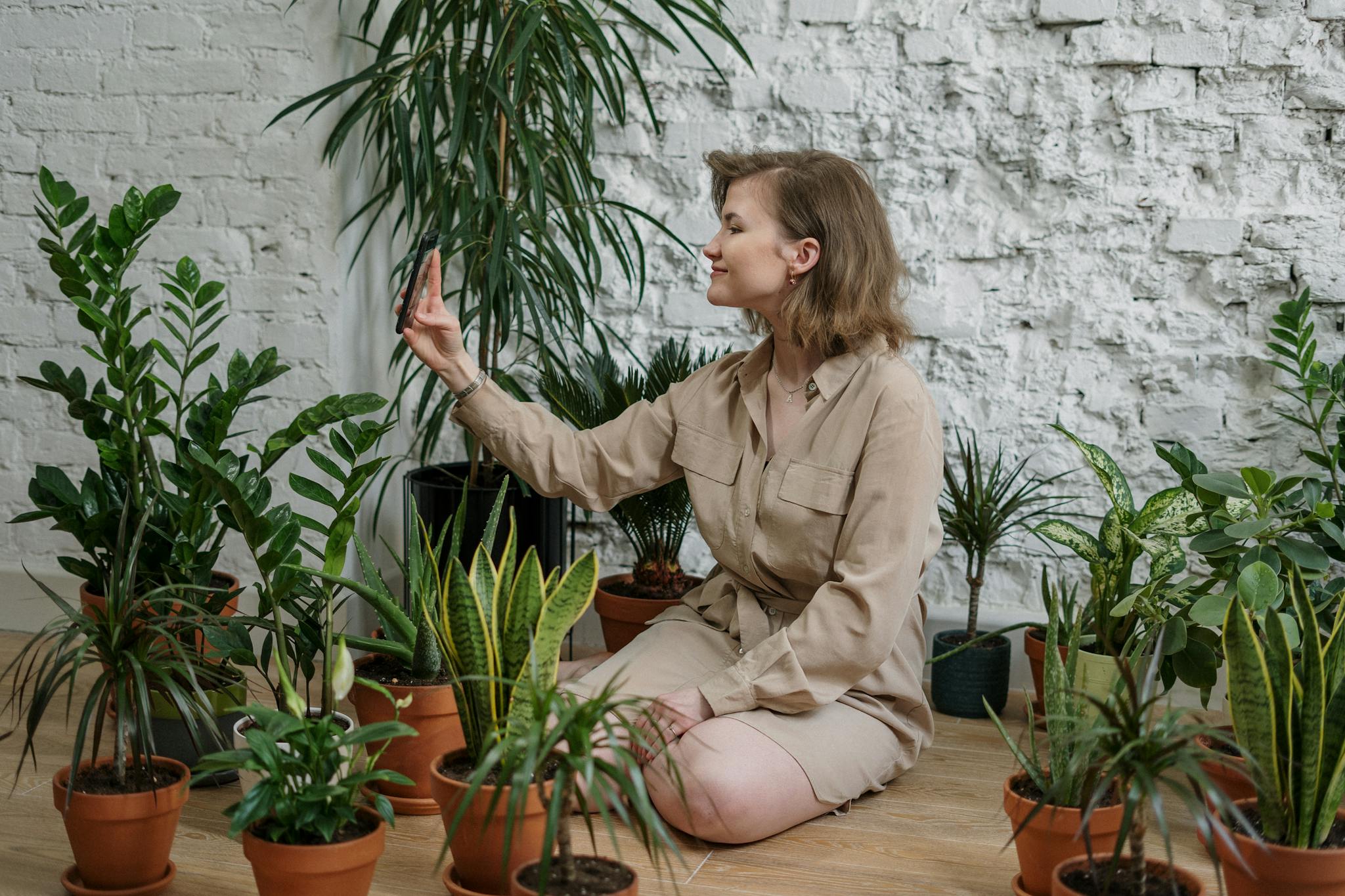 A woman takes a selfie while surrounded by various potted houseplants indoors.